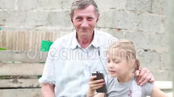 爷爷和孙女在公园里听着耳机里的音乐手里拿着手机跳舞视频的预览图