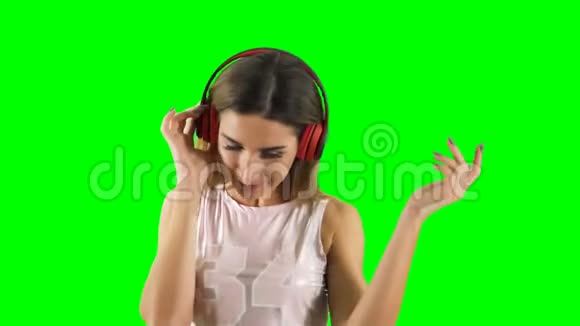 戴着耳机的快乐女孩在绿色背景下听音乐跳舞视频的预览图