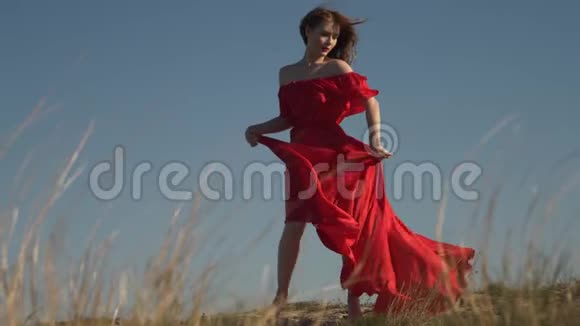 穿着猩红衣服的年轻女子模特穿着风装在日落时赤脚视频的预览图