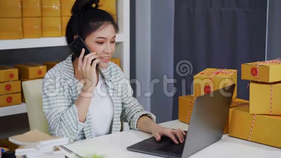 女人在智能手机上讲话用电脑手提电脑从家庭办公室在线销售产品视频的预览图