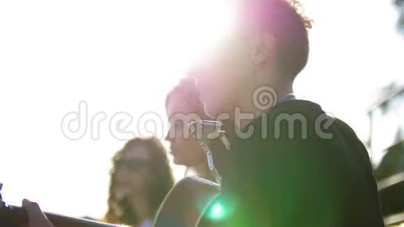 年轻的白种人朋友在夏天的公园里玩在日落时用吉他唱歌视频的预览图