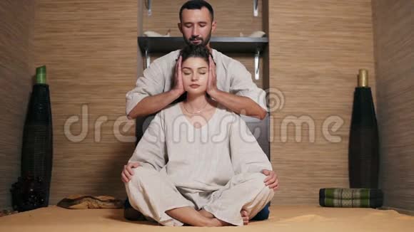 吸引人的泰国按摩师正在按摩坐在她身后年轻女子的头美丽的女孩闭着眼睛视频的预览图