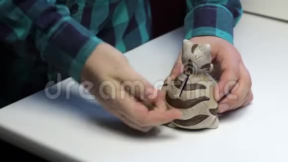 桌子上是一只猫形的储蓄罐一个人手里拿着硬币放在储蓄罐里视频的预览图