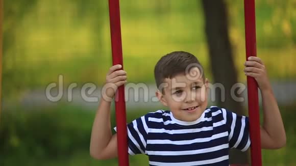 一个穿着条纹t恤的小男孩正在操场上玩耍在秋千上荡秋千春天视频的预览图