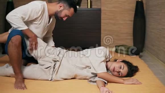 泰国男性按摩师正在治疗年轻女性臀部和坐骨神经握住她的腿并伸展它们泰式按摩视频的预览图