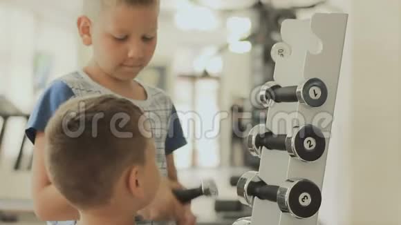 大一点的男孩帮助小一点的人在健身房锻炼时选择哑铃视频的预览图