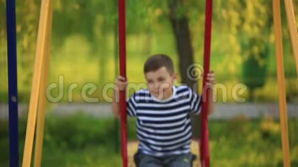 一个穿着条纹T恤的小男孩正在操场上玩在秋千上荡秋千春天视频的预览图