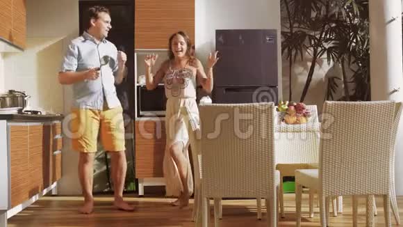 年轻迷人的快乐夫妇在阳光明媚的早晨在厨房做饭时玩着跳舞唱歌的乐趣3840x2160视频的预览图
