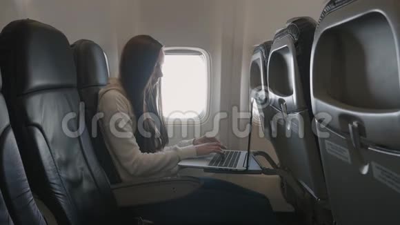 坐在靠近窗户的飞机上用笔记本电脑的女孩视频的预览图