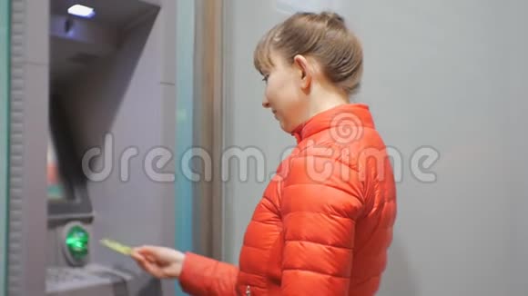 女人用提款机漂亮的年轻女性穿着红色泡沫外套在自动取款机上插入信用卡然后进入密码视频的预览图