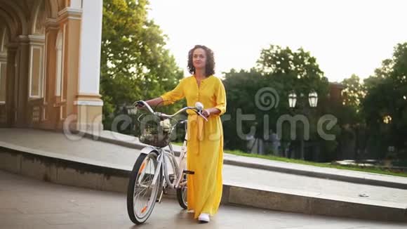 微笑着的年轻女孩穿着一件黄色的长裙手里拿着自行车车把篮子里放着鲜花视频的预览图