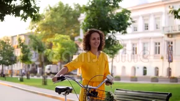 穿着黄色长裙的迷人女子微笑着手里拿着自行车车把篮子里放着鲜花视频的预览图