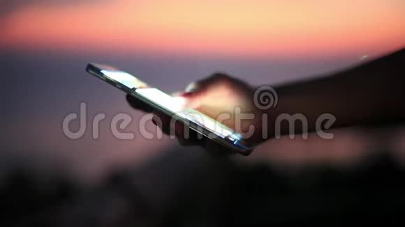 人类手在日落海滩海边使用移动智能手机有模糊的bokeh灯1920x1080视频的预览图