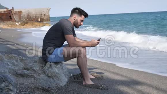 一个坐在沙滩巨石上忙着打电话的人视频的预览图