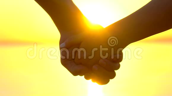 浪漫幸福夫妇的剪影两个情人年轻的男人和女人在日落时牵手在海洋海岸特写视频的预览图