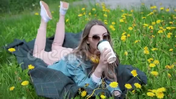 美丽的年轻女子喜欢喝咖啡躺在草地上喝咖啡的女人视频的预览图