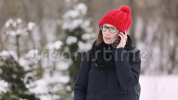 戴着眼镜和一顶红色针织帽子的白种人女孩和一个男人在手机上交谈时尚女人用粉色视频的预览图