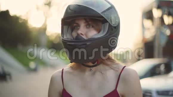 美丽的年轻红发女摩托车手在夕阳下摘下头盔视频的预览图