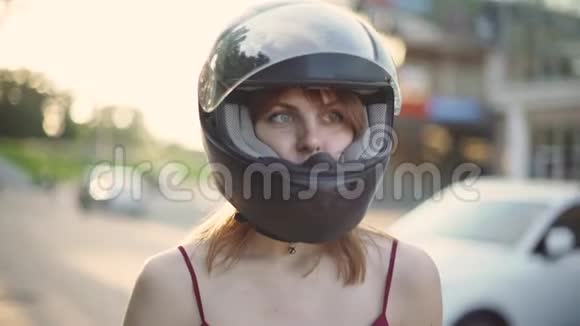 美丽的年轻红发女摩托车手在夕阳下摘下头盔视频的预览图