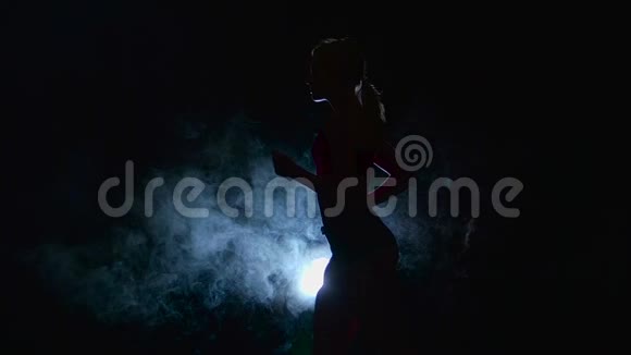 运动员在烟雾中被聚光灯照亮的黑色背景上轻轻地奔跑剪影慢动作视频的预览图