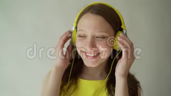 美丽的微笑布鲁内特听音乐使用耳机在工作室的灰色背景视频的预览图