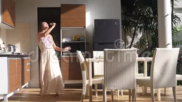 快乐的年轻女人在阳光明媚的早晨一边在厨房唱歌跳舞一边做早餐60fps慢动作视频的预览图
