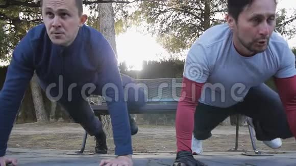 与户外私人教练一起健身两名男性运动员在公园里一起做板膝肘运动视频的预览图