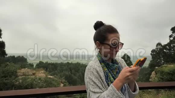 4k灰色女孩在绿色的田野山丘棕榈园木头和手的农村背景下输入智能手机视频的预览图
