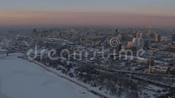空中无人驾驶飞机在日落时俯瞰河岸积雪覆盖的城市视频的预览图