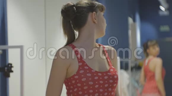 年轻女子在试穿衣服漂亮的白种人女性看着镜子转过身来穿着红色衬衫视频的预览图