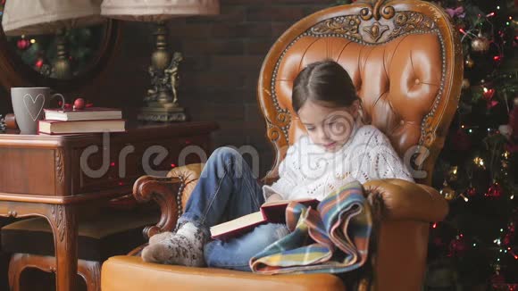 女孩在圣诞树旁的扶手椅上读童话视频的预览图