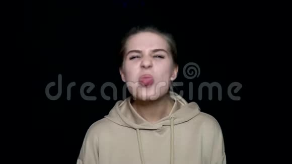 一个年轻女子做着滑稽的脸用舌头戏弄被隔离在黑色背景下疯狂美女视频的预览图