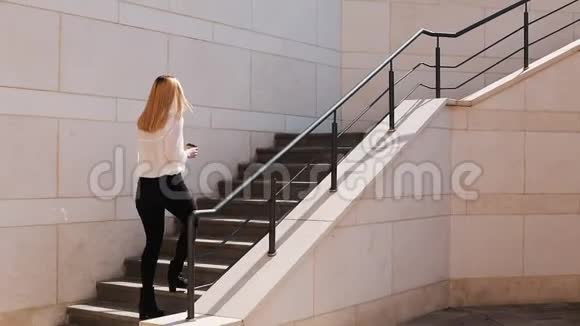 年轻的金发商务女性在阳光明媚的一天在办公楼附近走上楼视频的预览图