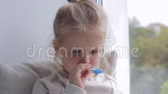 年轻生病的女孩测量窗户附近的温度她嘴里拿着体温计视频的预览图