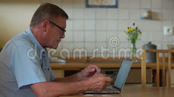 退休人员互联网技术一位老人坐在厨房的桌子旁正在用他的笔记本电脑工作他是视频的预览图