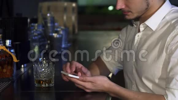 在酒吧喝酒的时候一个男人用他的智能手机在酒吧里紧紧抓住视频的预览图