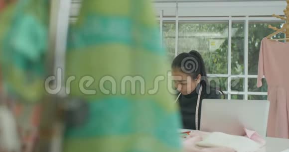 漂亮的时装设计师坐在她的办公桌前看着现代工作室笔记本电脑上的草图视频的预览图