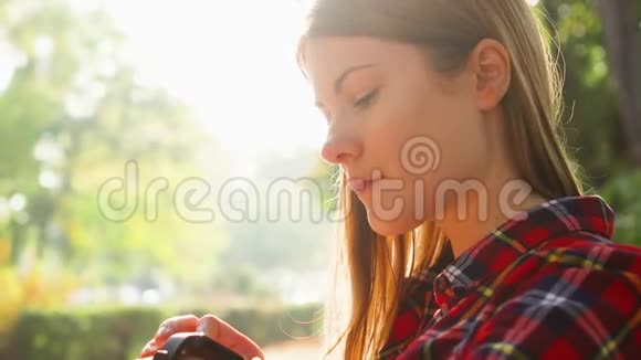 微笑的女人享受大自然坐在绿色公园的长凳上用智能手表口述信息视频的预览图