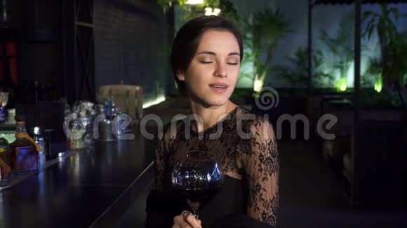 漂亮的年轻女子坐在酒吧旁手里拿着一杯酒微笑着对着镜头视频的预览图
