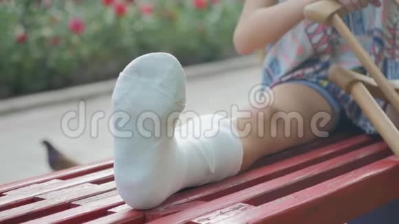 腿断的女孩坐在长凳上在描述垫的背景上看着智能手机视频的预览图