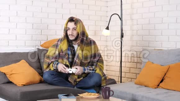 高加索人坐在毯子下面的沙发上玩游戏机50fps视频的预览图