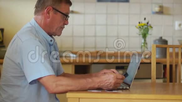 一位老人拿着电脑和电话工作坐在厨房的桌子旁视力和防护眼镜视频的预览图