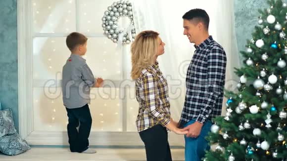 当他们的儿子在窗台上等圣诞老人的时候快乐的爸爸妈妈在圣诞树附近聊天视频的预览图