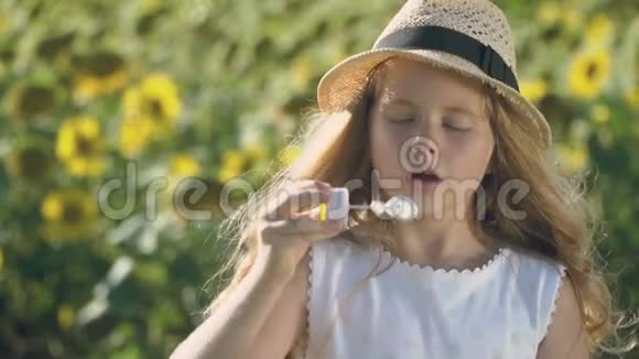 戴帽子的快乐小女孩在向日葵的背景下吹泡泡视频的预览图