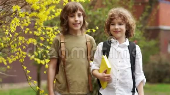 两个男孩拥抱看着相机学校的朋友们在笑孩子们后面有书包回到学校视频的预览图