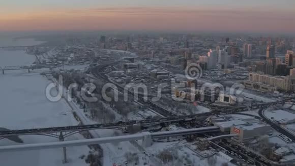 空中无人驾驶飞机在日落时俯瞰河岸积雪覆盖的城市视频的预览图