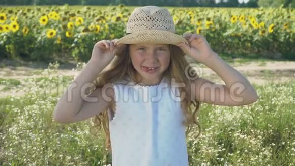 戴帽子的小女孩在向日葵背景下鬼脸的肖像视频的预览图