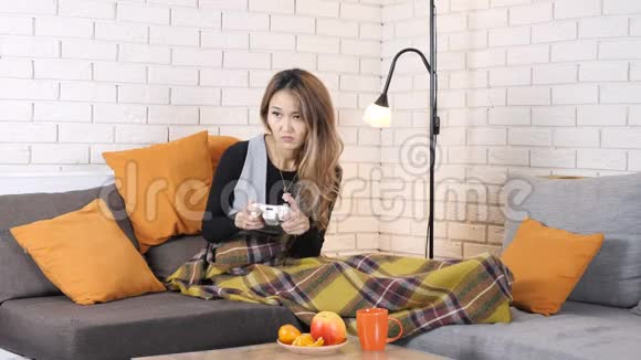 悲伤的亚洲女孩坐在沙发上的毛毯下玩游戏机输了50帧秒视频的预览图