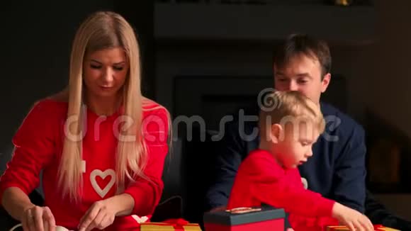 家人在圣诞节时爸爸妈妈和儿子在家里打开礼物坐在圣诞节室内的沙发上温暖舒适视频的预览图