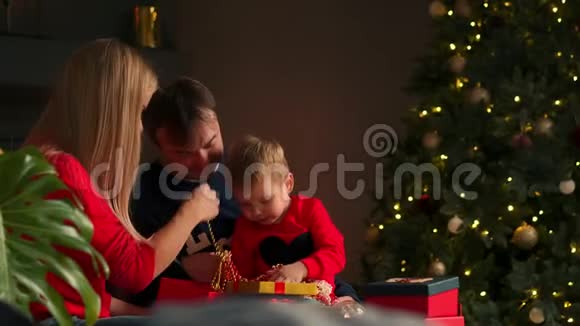 在圣诞节爸爸妈妈和儿子在家里打开礼物坐在圣诞内部的沙发上温馨舒适的家视频的预览图